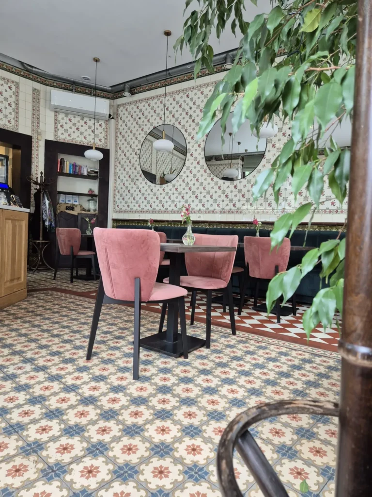 Krzesła tapicerowane w pudrowym różu przy stoliku, na tle kaflowej ściany i wzorzystej posadzki w Kaffel w Gliwicach