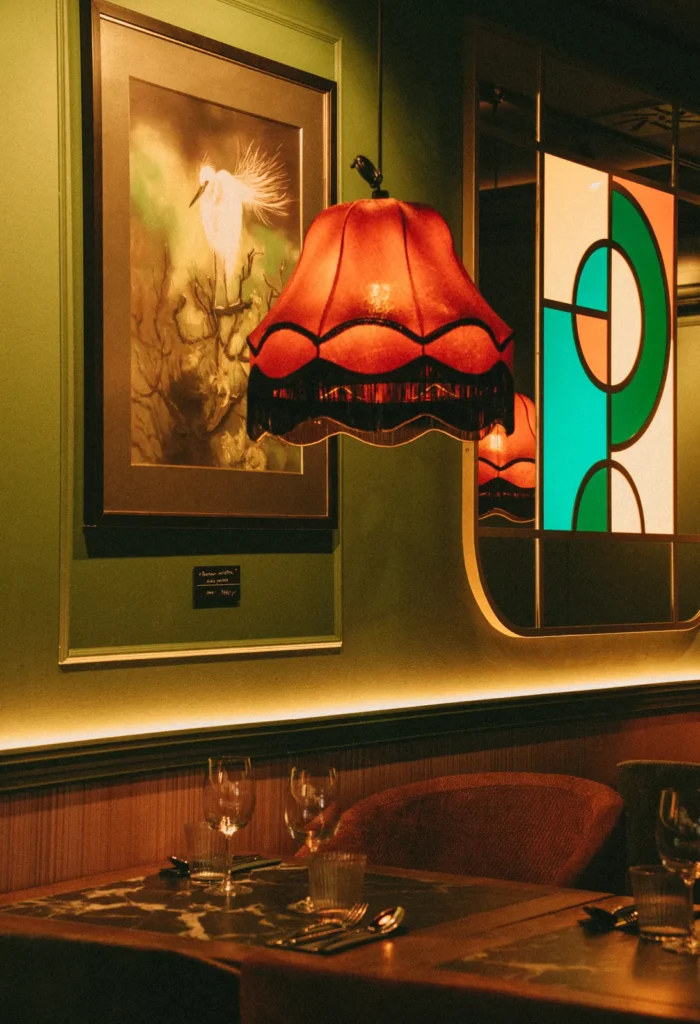 Sofa tapicerowana i krzesło pod zieloną ścianą z witrażowym lustrem w restauracji Restbotanica w Katowicach